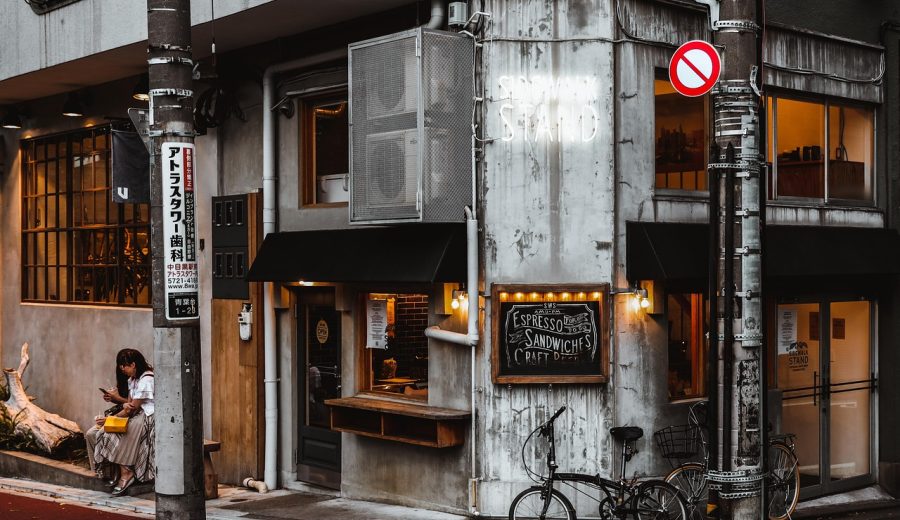 咖啡馆门口的木质招牌与手绘风格店名图形，清晨斜射光落在招牌表面，旁边摆着绿植，呈现小店常见的标志使用环境
